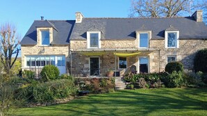 A stone house with a sloped roof, a covered porch, and a well-maintained garden. - Quiet and seaside in charming house 3000 m2 park (Créhen)