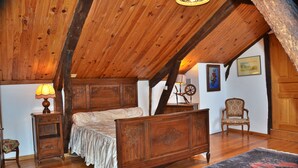 A bedroom with a wooden ceiling, a bed with a white bedspread, a nightstand with a lamp, a chair, and a rug.