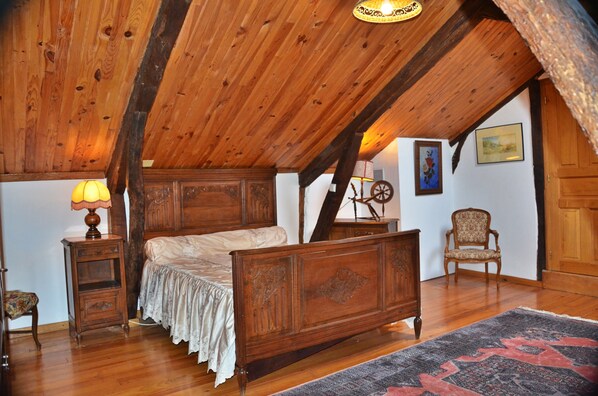 Une chambre avec un plafond en bois, un lit recouvert d’une courtepointe blanche, une table de chevet avec une lampe, une chaise et un tapis.