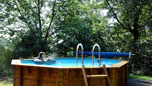 An above-ground wooden swimming pool with a ladder, surrounded by lush greenery.