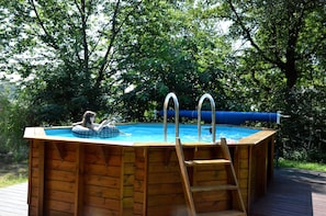 Una piscina de madera sobre el suelo, con una escalera, rodeada de exuberante vegetación.