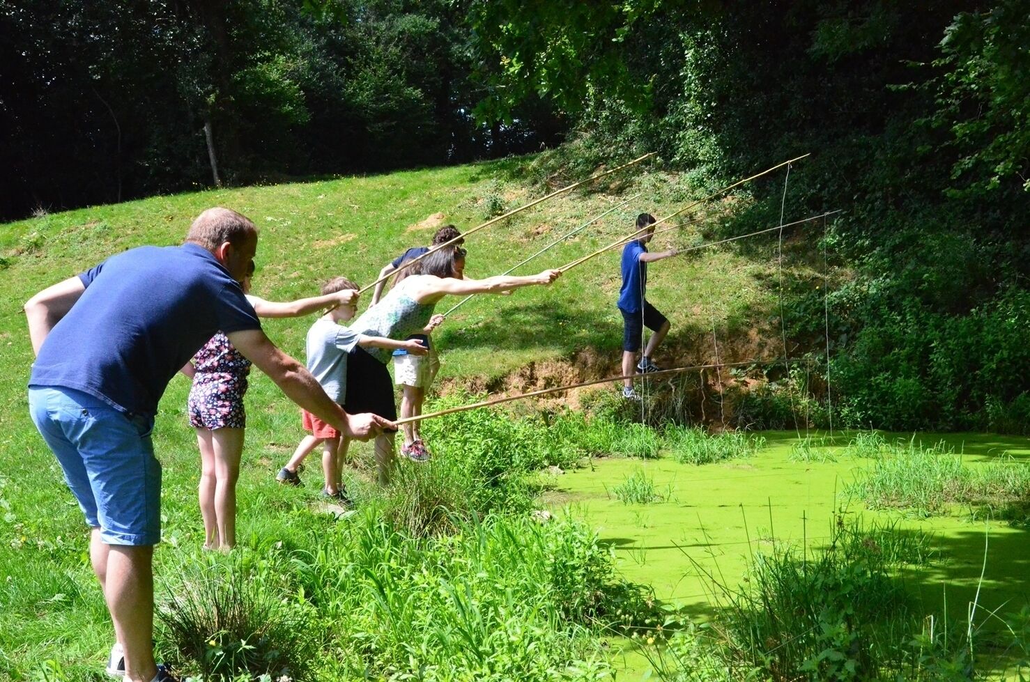 A group of people crossing a rope bridge over a green body of water in a natural setting.