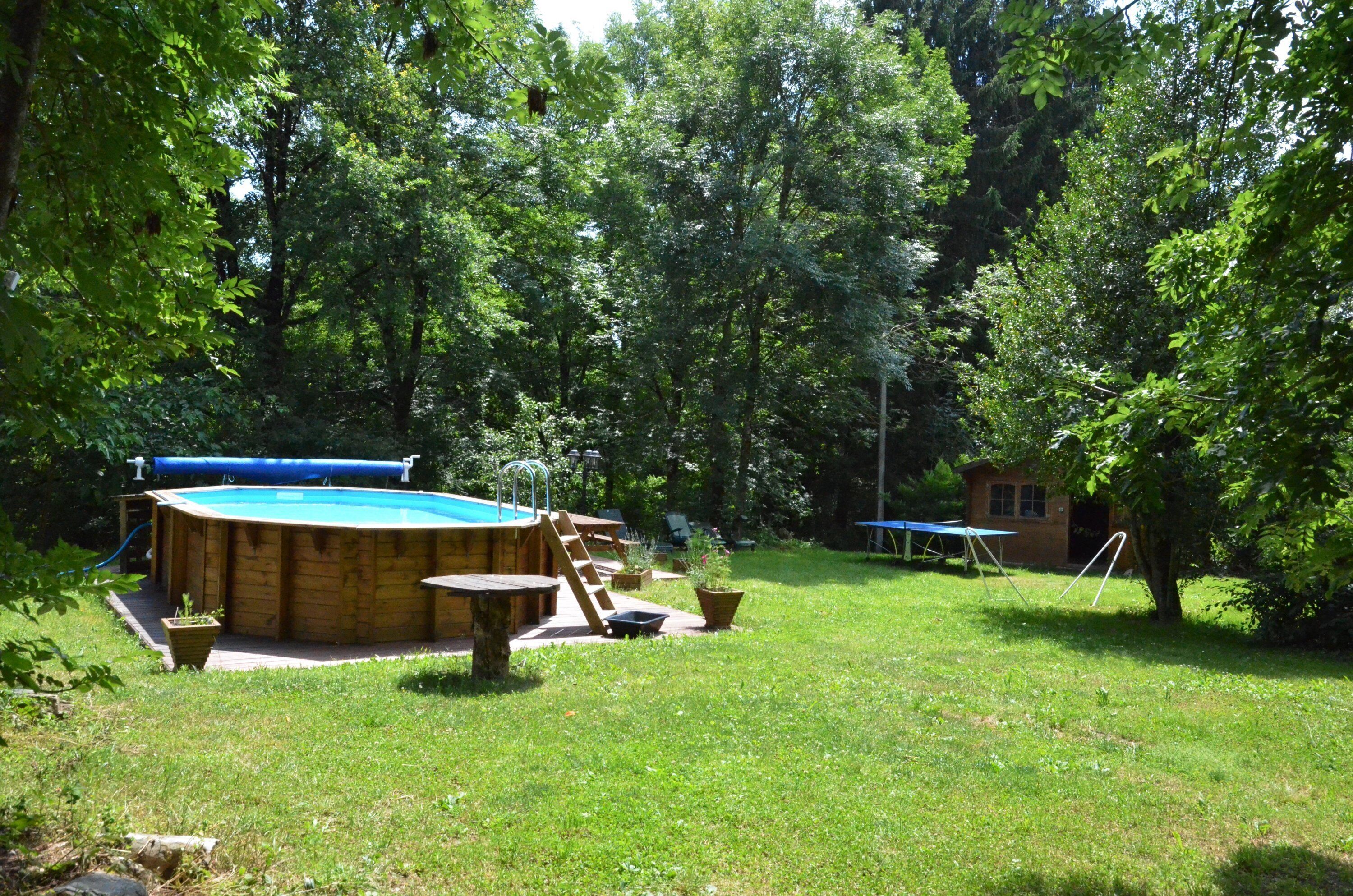 A wooden swimming pool with a ladder, surrounded by a grassy yard and trees.