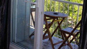 Un balcon avec une table et des chaises, une porte-fenêtre coulissante et une vue sur les bâtiments et les arbres.