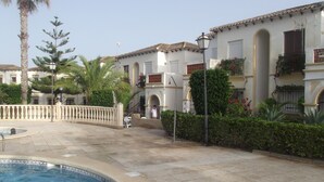 A pool area with a tiled deck, a palm tree, and a building with arched windows and balconies. - Apartment by the pool (SAN MIGUEL DE SALINAS)