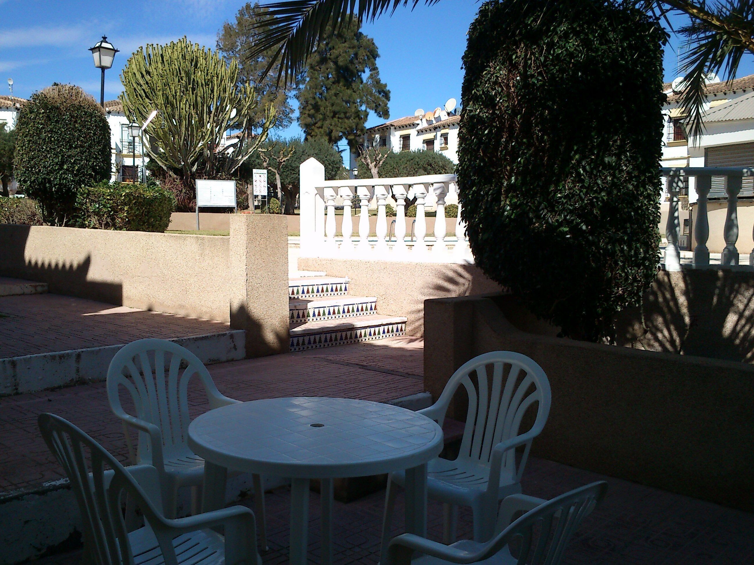 A patio with a round table and four chairs, surrounded by a low wall and various plants.