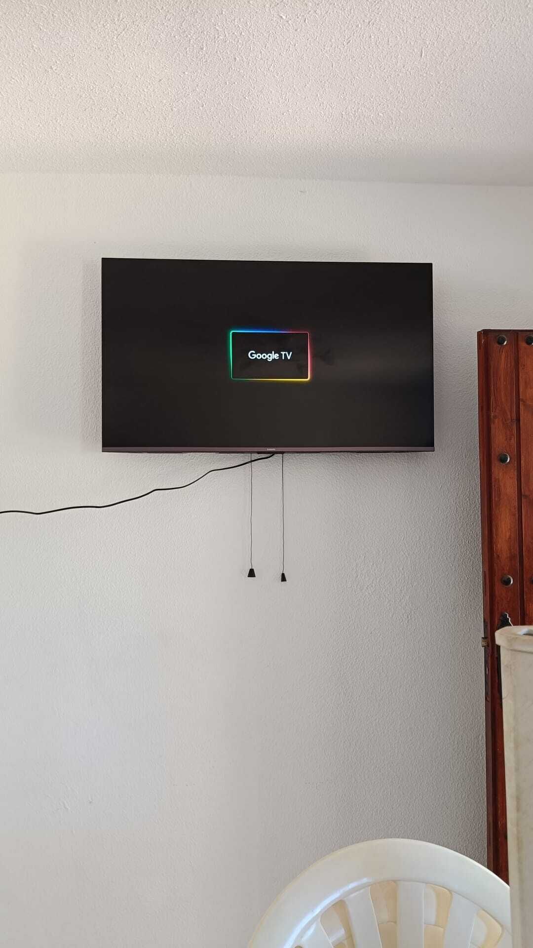 Un téléviseur à écran plat fixé au mur, avec un câble d’alimentation visible et une étiquette indiquant « Google TV ».