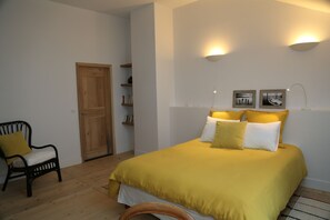 A bedroom with a large bed, a wooden door, a chair, and wall-mounted lights.