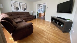 Una sala de estar con un sofá modular, piso de madera, televisor de pantalla plana y obras de arte en la pared.