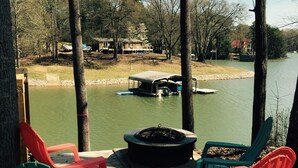 A deck with Adirondack chairs overlooking a lake, a dock with boats, and a fire pit. - Fantastic house, dock, water toys and hot tub!! Summer dates available!! (Catawba)