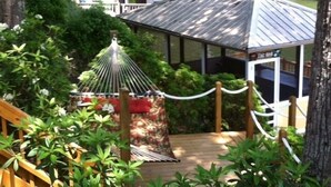 A wooden deck with a hammock, surrounded by lush greenery and a small gazebo. - Fantastic house, dock, water toys and hot tub!! Summer dates available!! (Catawba)