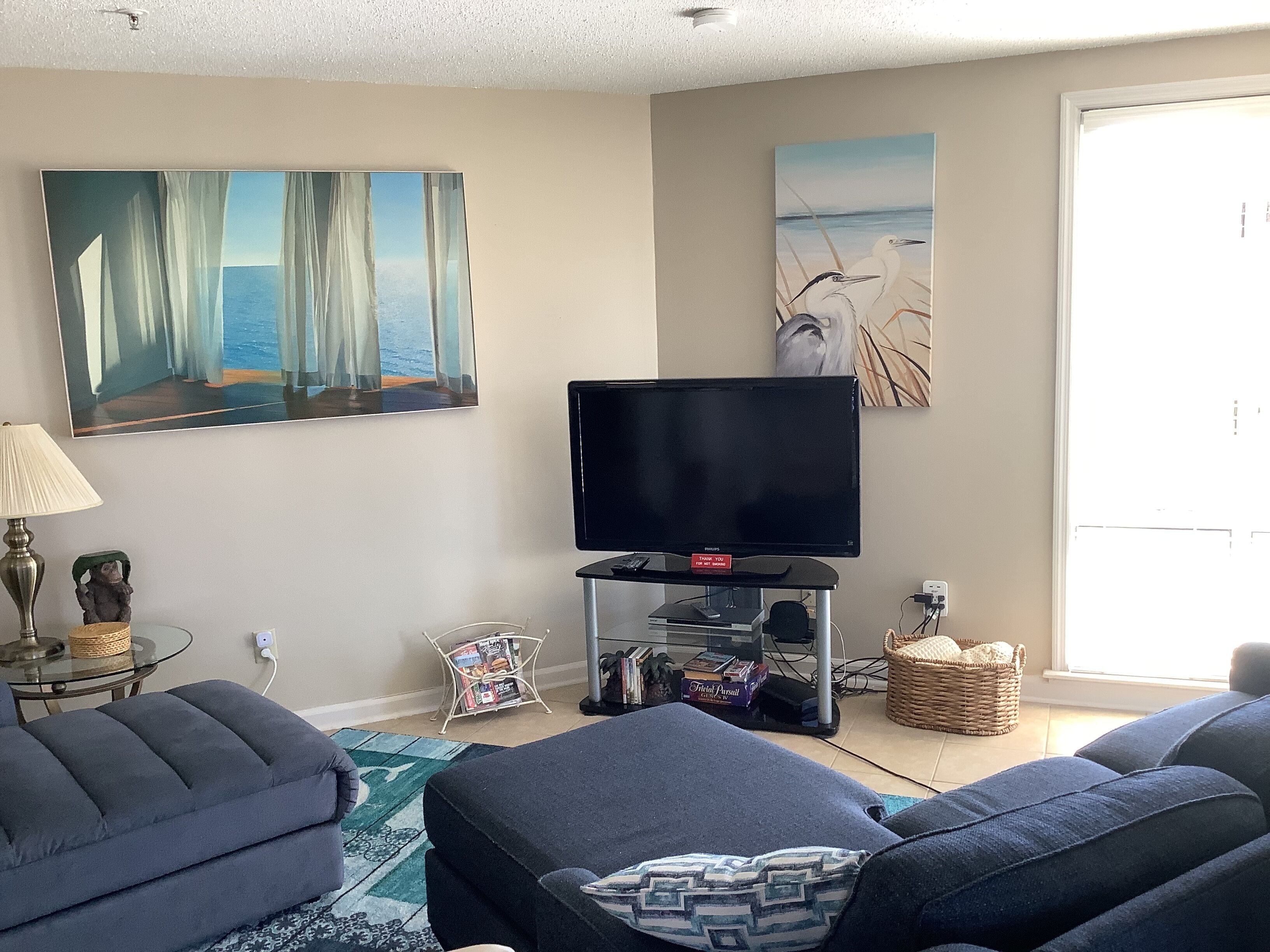 A living room with a flat-screen TV, a sofa, a lamp, and artwork on the walls.