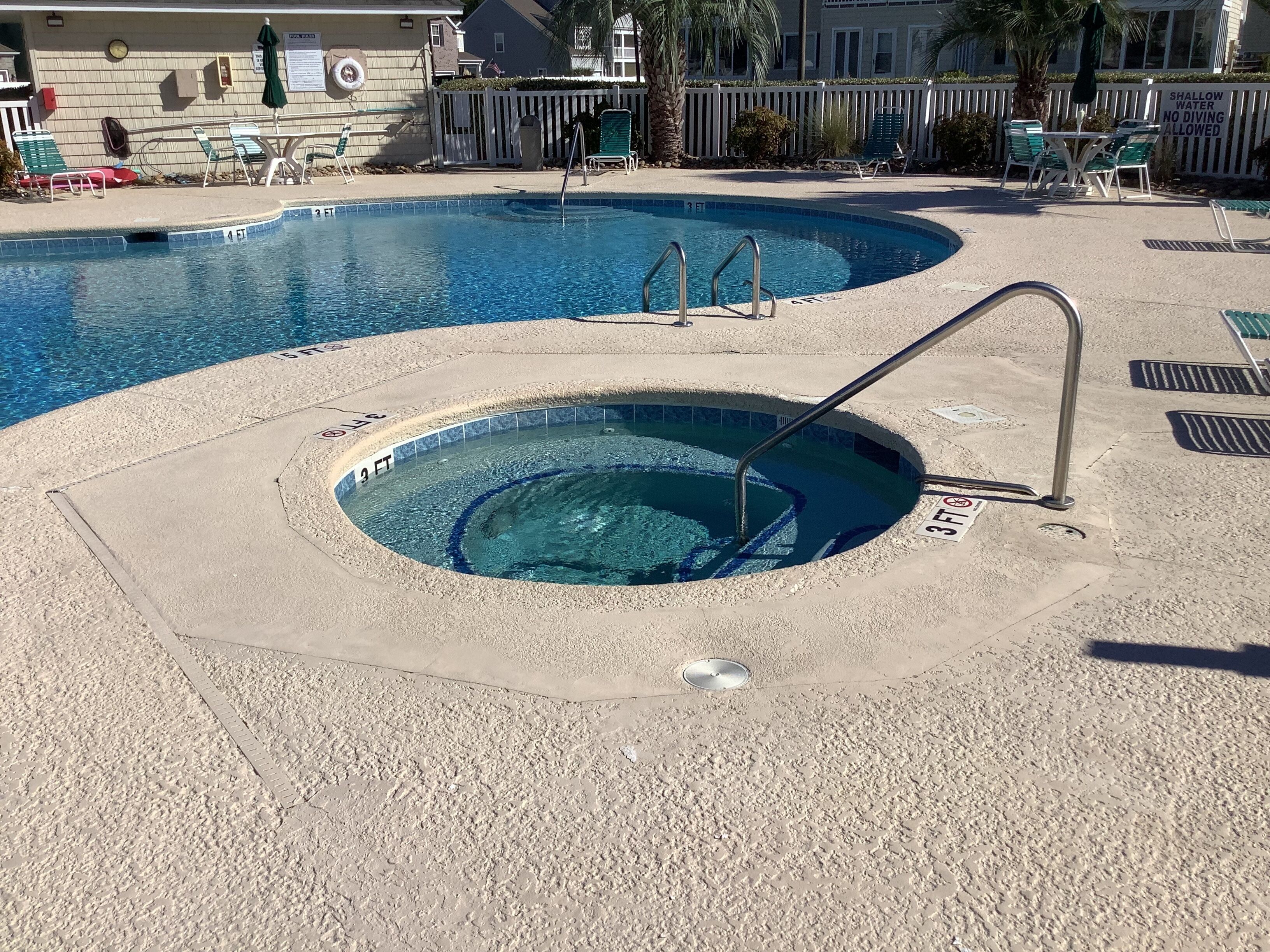 A swimming pool with a hot tub, lounge chairs, and a shallow water sign.