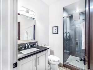 Ein modernes Badezimmer mit Waschbecken, Spiegel, Toilette und Duschkabine aus Glas.