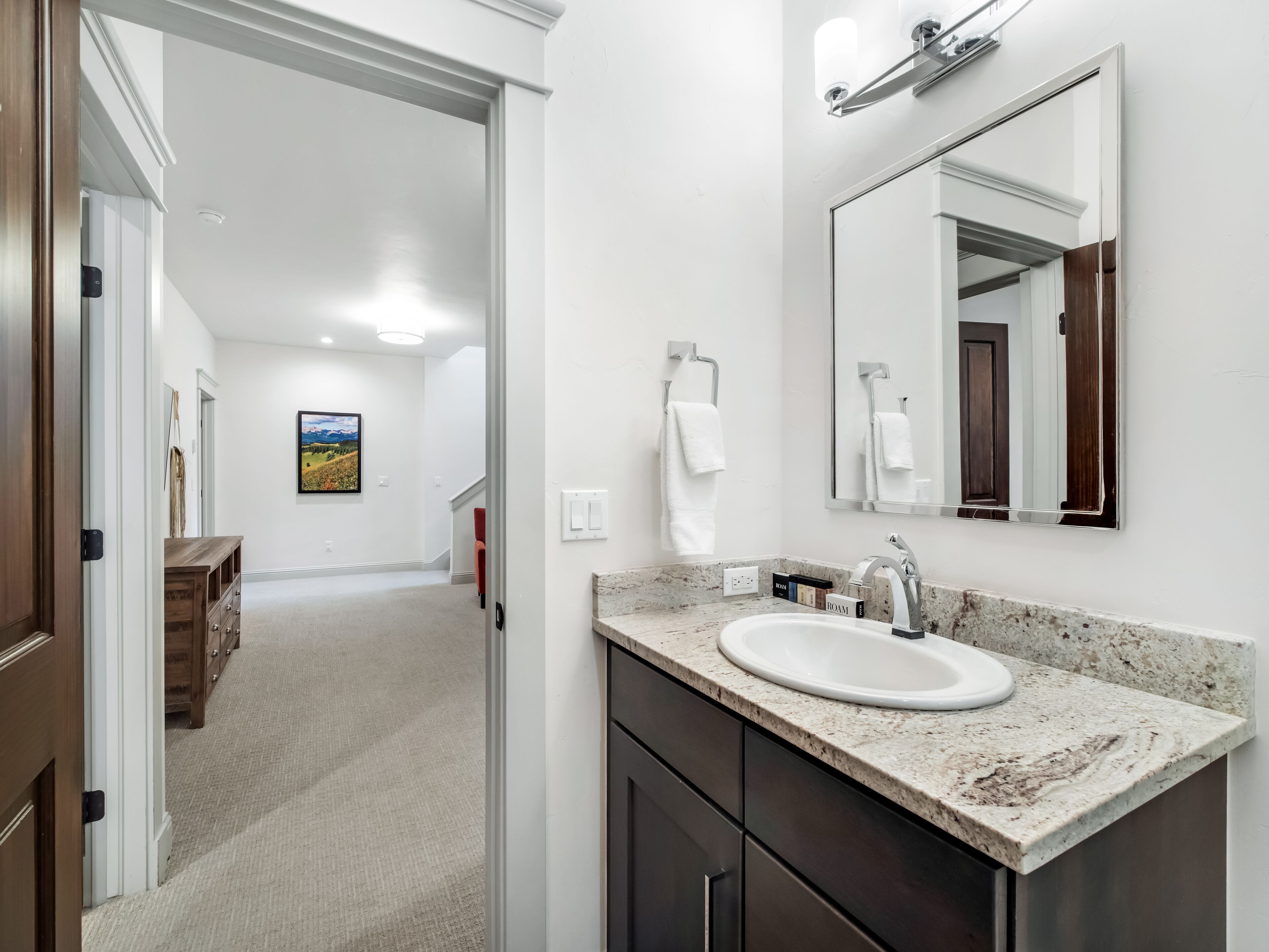 A modern bathroom with a white sink, dark cabinets, and a large mirror.