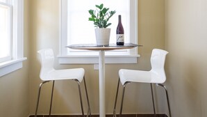 Un pequeño comedor con una mesa blanca, dos sillas blancas, una planta en maceta y una botella de vino.