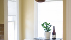 Cocina en esquina con una mesa blanca, dos taburetes blancos, una planta en maceta y una botella de vino.