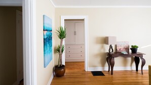 Un pasillo con piso de madera, una puerta, una planta en maceta, una mesa con lámpara y obras de arte en la pared.