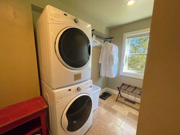 Une buanderie équipée d’une machine à laver et d’un sèche-linge superposés, d’un étendoir et d’une fenêtre donnant sur les arbres.