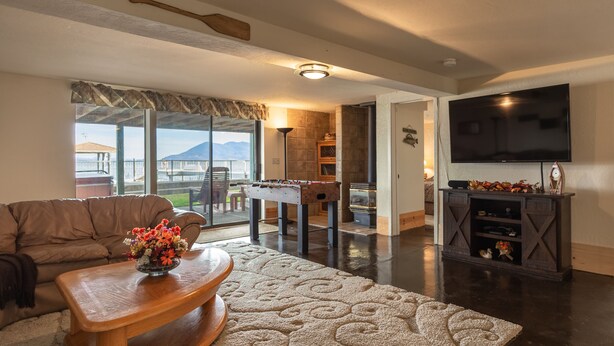 A living room with a sofa, coffee table, and a foosball table. There is a TV mounted on the wall and a fireplace.