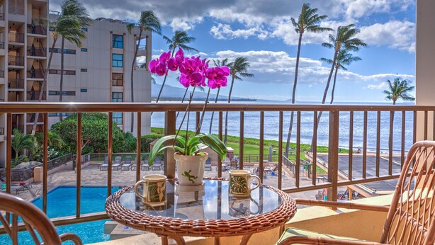 Un balcón con vistas al océano, una piscina y plantas tropicales.