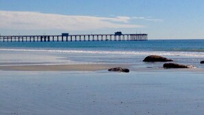 A beach with a pier extending into the water, rocks near the shore, and a clear sky.