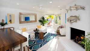 A spacious living room with a wooden dining table, white sofas, a patterned rug, and a fireplace.
