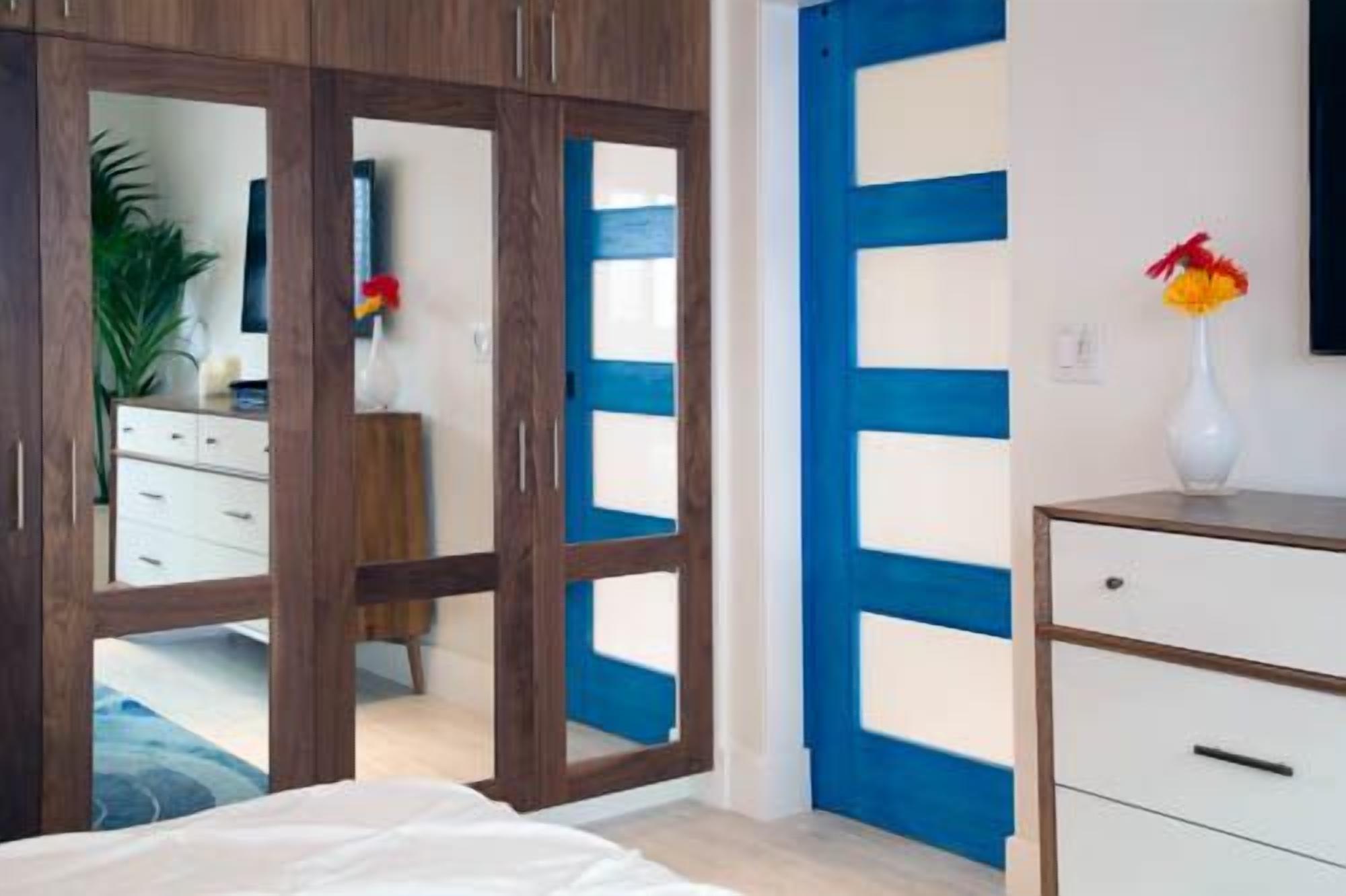 Un dormitorio con cama, cómoda, espejo y una puerta azul y blanca.