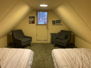 Ein kleines, dreieckiges Schlafzimmer im Dachgeschoss mit zwei Einzelbetten, einem Heizgerät und einer Tür mit Fenster.