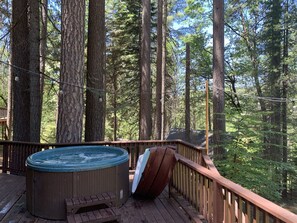Ein Whirlpool auf einer Holzterrasse, umgeben von hohen Bäumen.