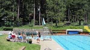 A swimming pool with a stone wall, surrounded by a grassy area and trees.