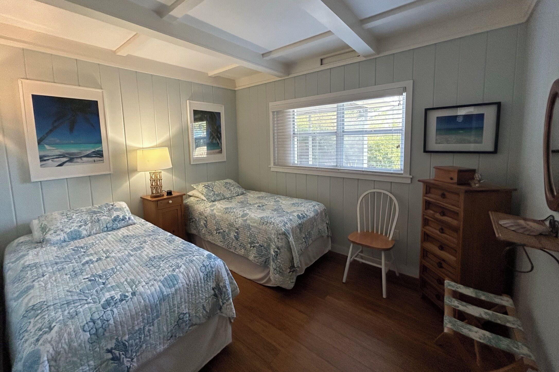 A bedroom with two beds, a chair, a dresser, and framed pictures on the walls.