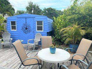 A blue house with two windows and a decorative wall piece, surrounded by potted plants and outdoor furniture. - 5 star Quiet, Comfy Home, Pets OK, Walk DTWN, Trolley to Beach ,Bike Legacy Trl (Sarasota)