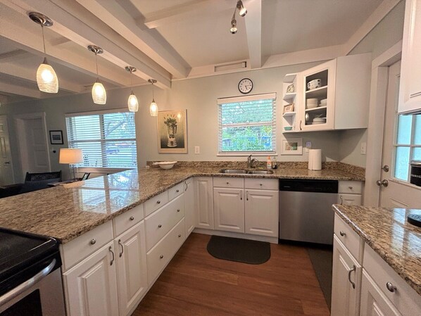 A kitchen with white cabinets, granite countertops, a dishwasher, and pendant lighting.
