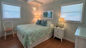 Quarto com uma cama, duas mesas de cabeceira, uma cadeira e uma janela com persianas.