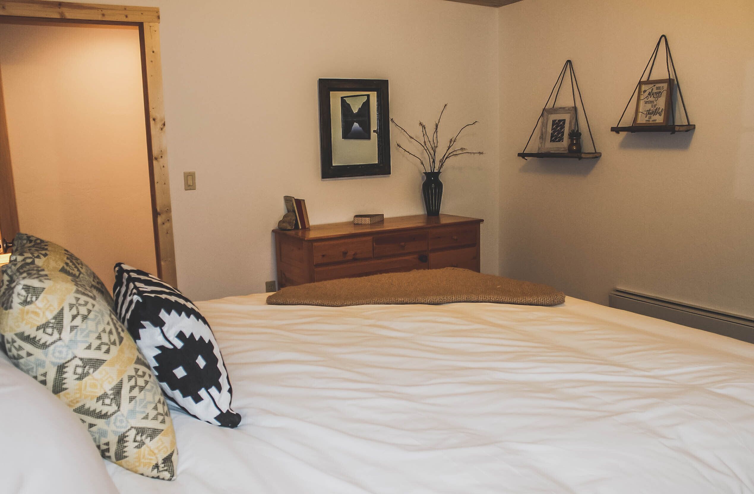 A bedroom with a bed, pillows, a dresser, and wall-mounted shelves.