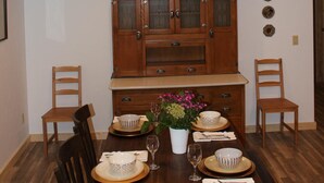 A dining room with a wooden ceiling, a wooden cabinet with glass doors, and a dining table set with plates, bowls, and a vase of flowers. - Mountain Retreat Condo (Kremmling)