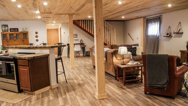 A spacious living area with a wooden floor, a kitchen with a central island, a staircase, and a cozy seating area with a lamp. - Mountain Retreat Condo (Kremmling)