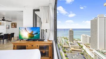 Ein Hotelzimmer mit großem Fernseher, Schreibtisch aus Holz und Blick auf Stadt und Meer.
