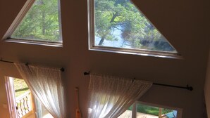 A room with a sloped ceiling, large windows, and a view of a wooden deck and trees. - Serene Setting on the Platte River (Honor)