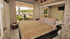 A bedroom with a bed, a bedside table, a window with curtains, and a view of the outside. - Jaco Beach awesome remodeled condo on the main strip. Walk to the beach and town (Jaco)
