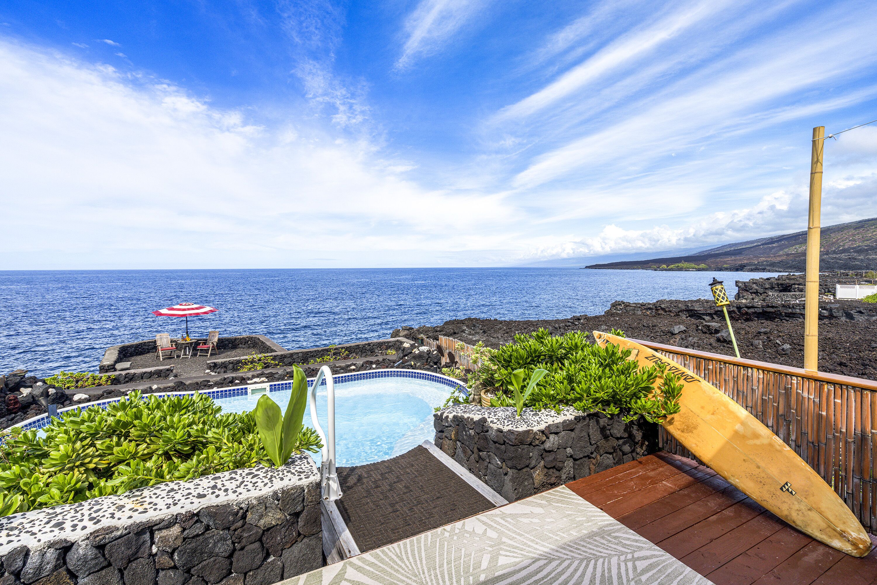 A pool with a view of the ocean, surrounded by plants and a wooden deck.