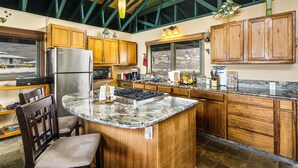 A kitchen with wooden cabinets, a granite countertop, a stainless steel refrigerator, and a large island with seating.