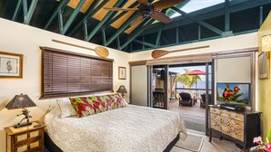 Un dormitorio con una cama, ventilador de techo, televisor y vistas al exterior.