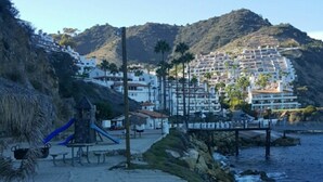 A sandy beach with a playground, a rocky shoreline, and buildings in the background. - MAGNIFICENT OCEAN VIEW Hamilton Cove Condo With Golf Cart Included. (Avalon)