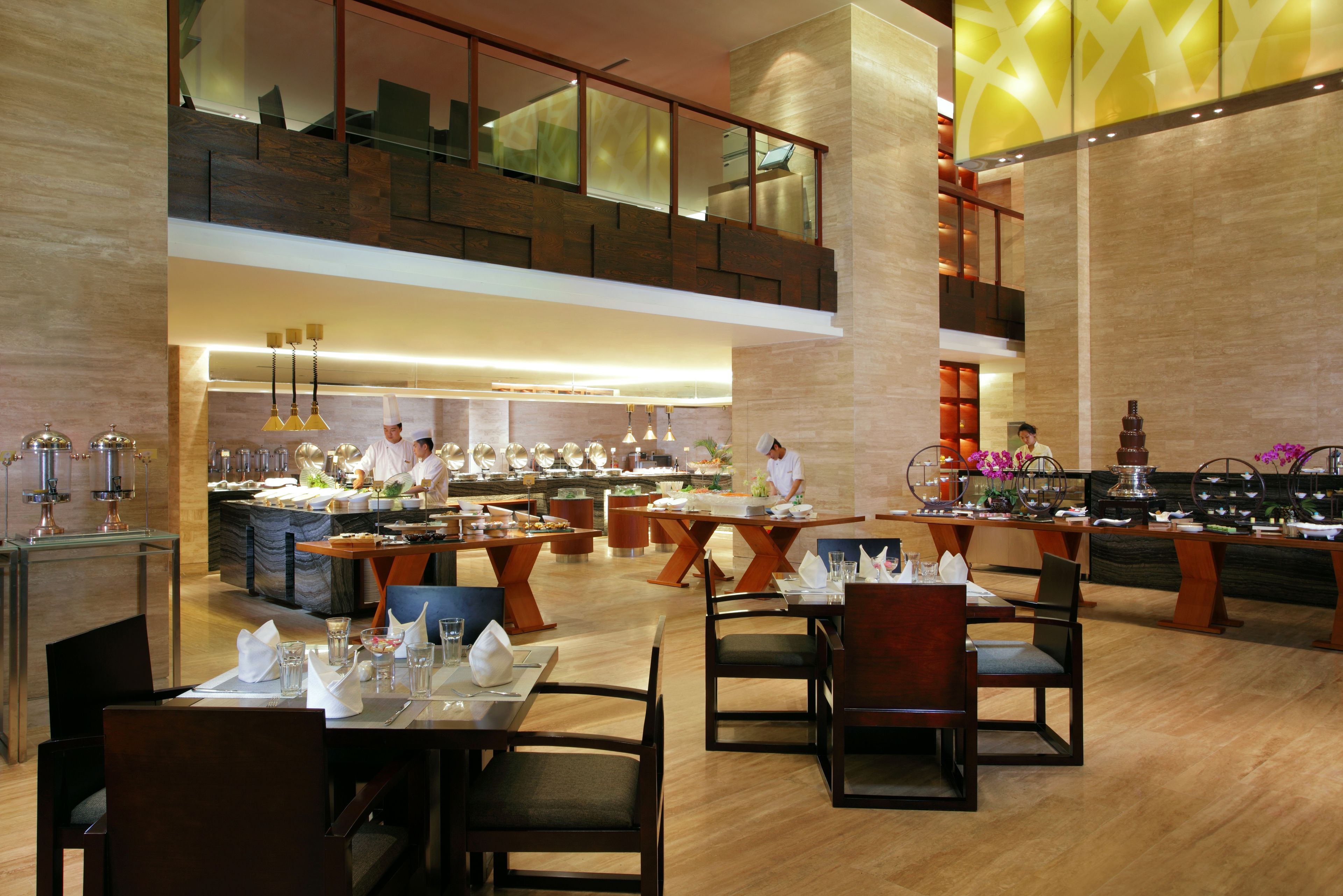 Amplia zona de comedor de hotel con varias mesas y sillas, un chef preparando comida y una decoración de diseño moderno.
