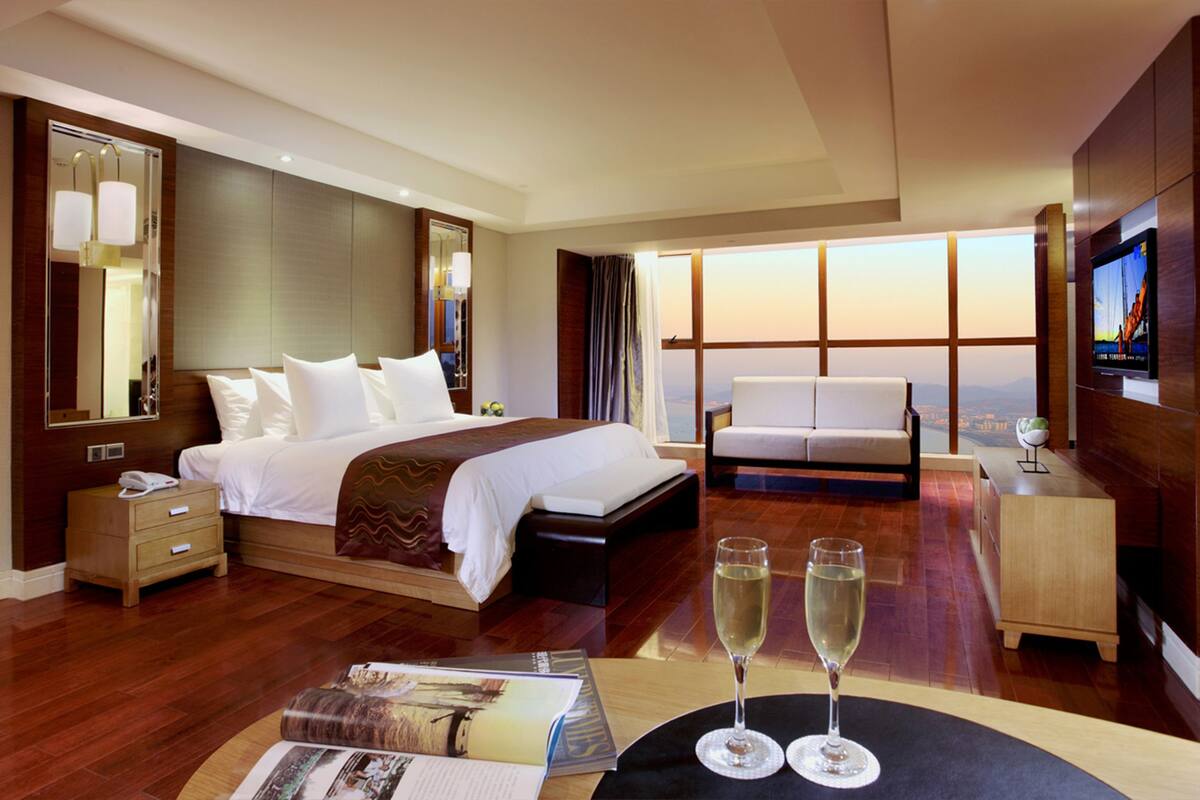 A hotel room with a large bed, a sofa, a TV, and a table with two glasses of champagne.