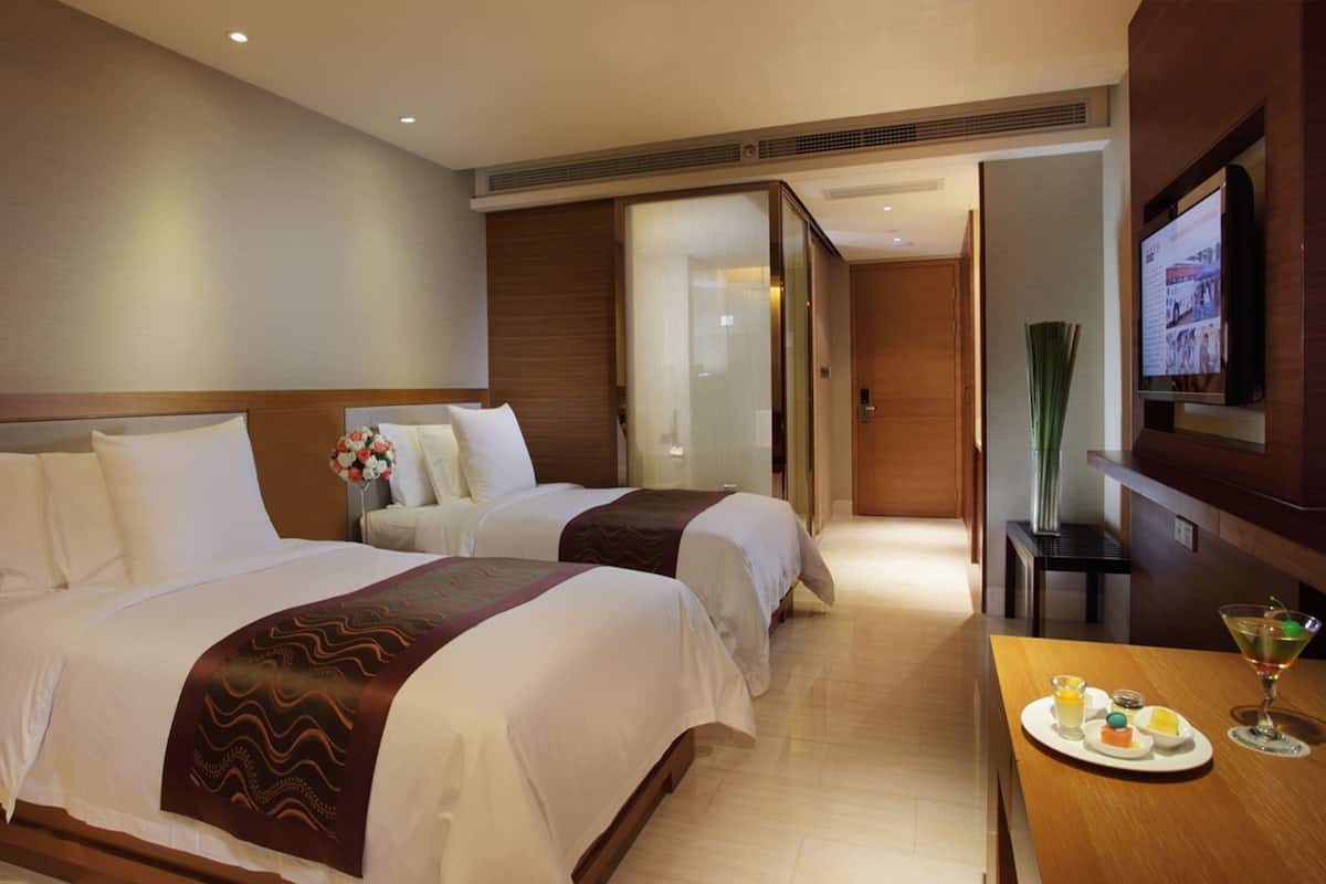 A hotel room with two beds, a TV, a dining table with a martini glass, and a vase of flowers.