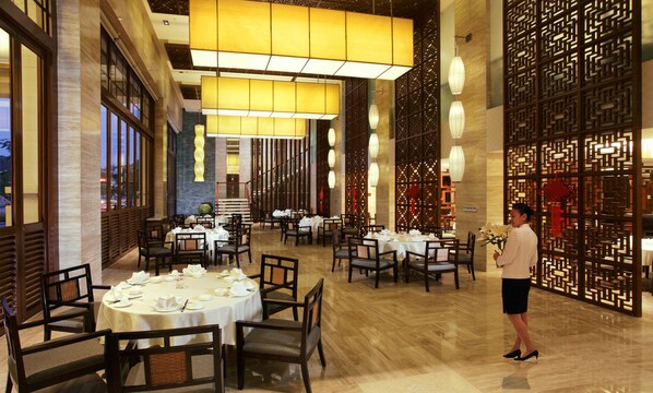 Un restaurante con mesas y sillas redondas, un camarero y decoración tradicional.