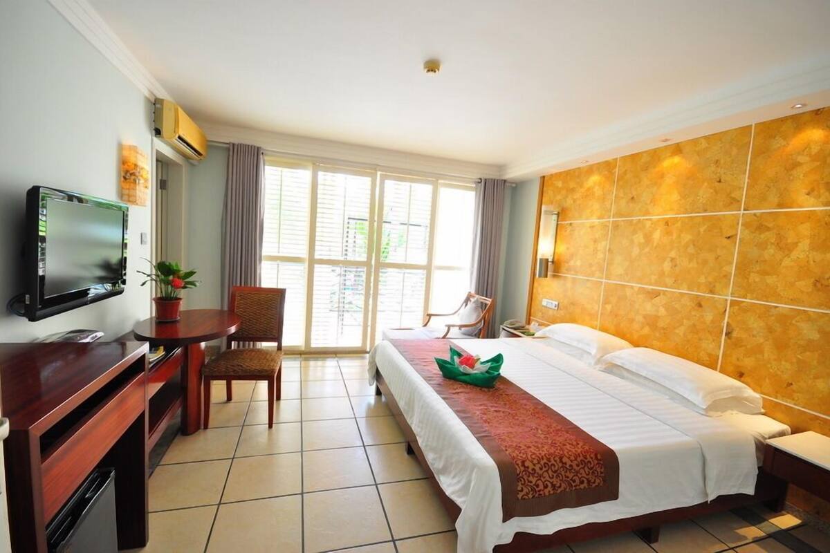 Quarto de hotel com cama, secretária com televisão, uma cadeira e janela com cortinas.